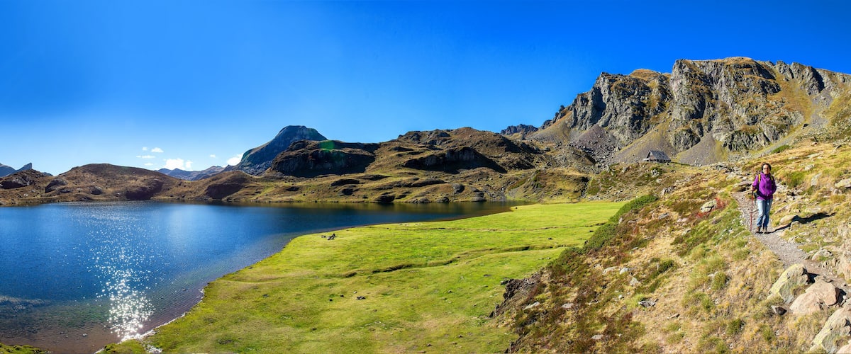 A mountainous landscape with a lake, a grassy area, and a person hiking.