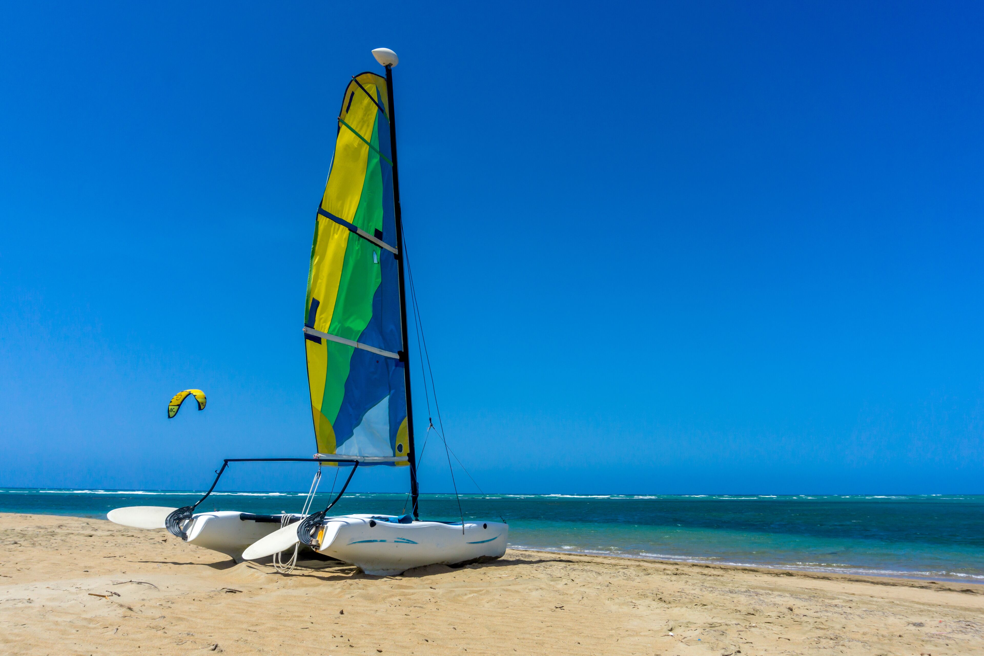 A beach with a sailboat and a parasail.