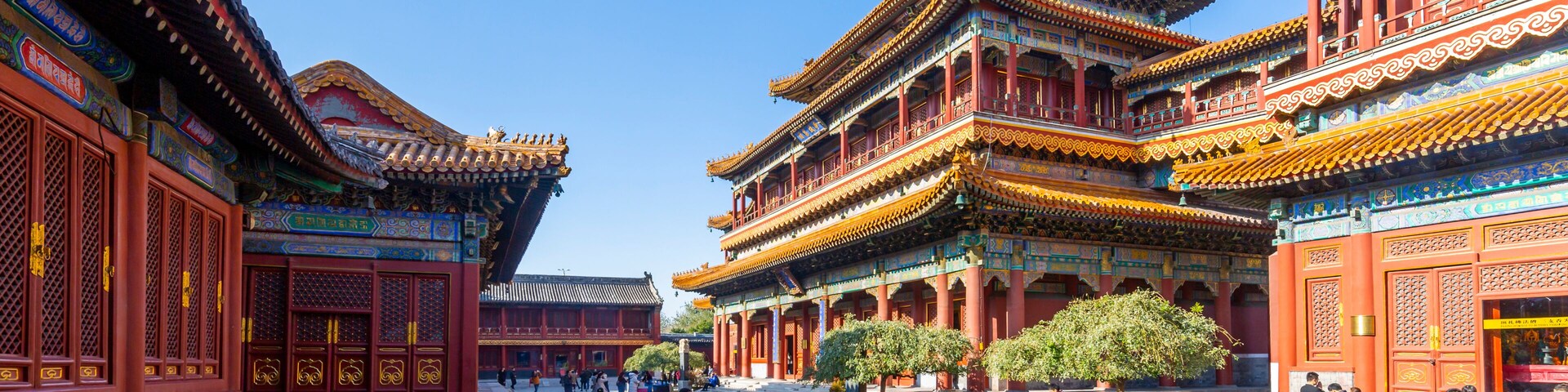 Um pátio tradicional chinês com edifícios ornamentados, céu azul límpido e pessoas passando.