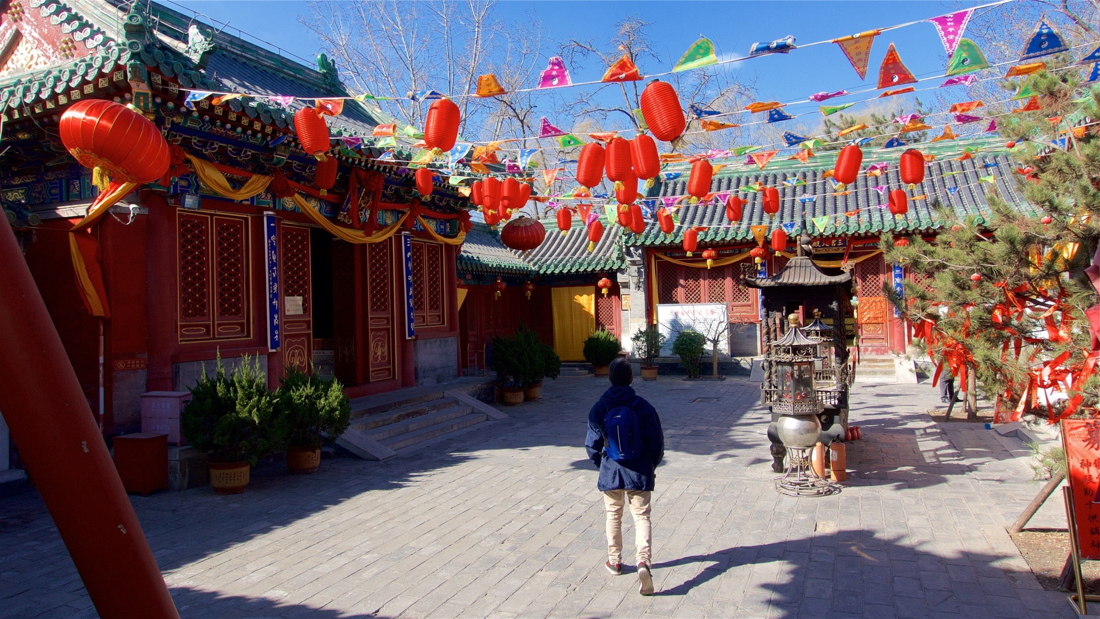 Um pátio tradicional chinês com lanternas vermelhas, bandeiras coloridas e arquitetura elaborada.