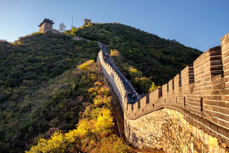 The Great Wall of China winding through a mountainous landscape with watchtowers and lush vegetation.