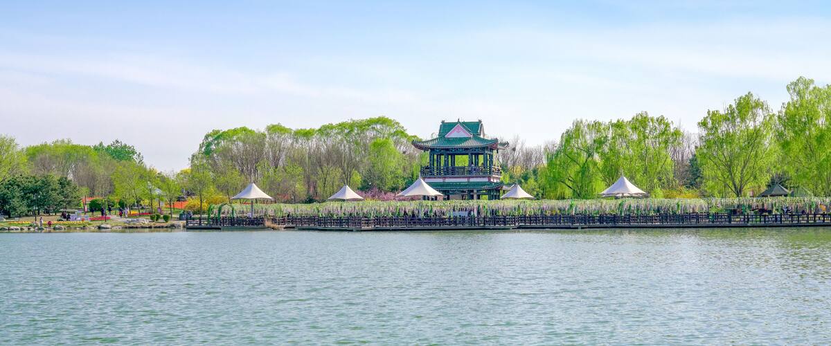 A serene lake with a traditional pavilion and trees in the background.
