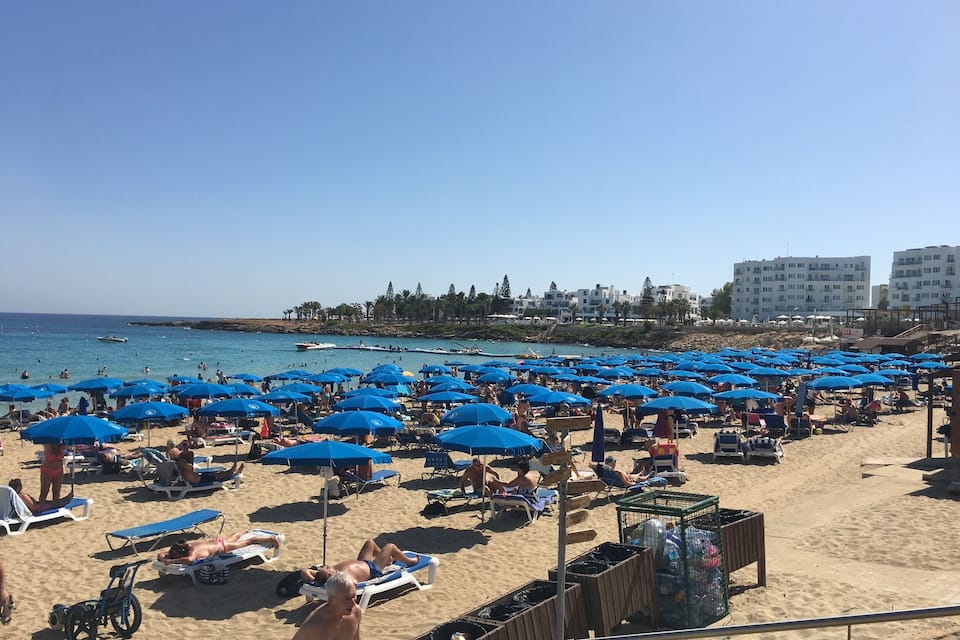 Una platja plena de gent, amb nombroses papereres i gandules blaves.