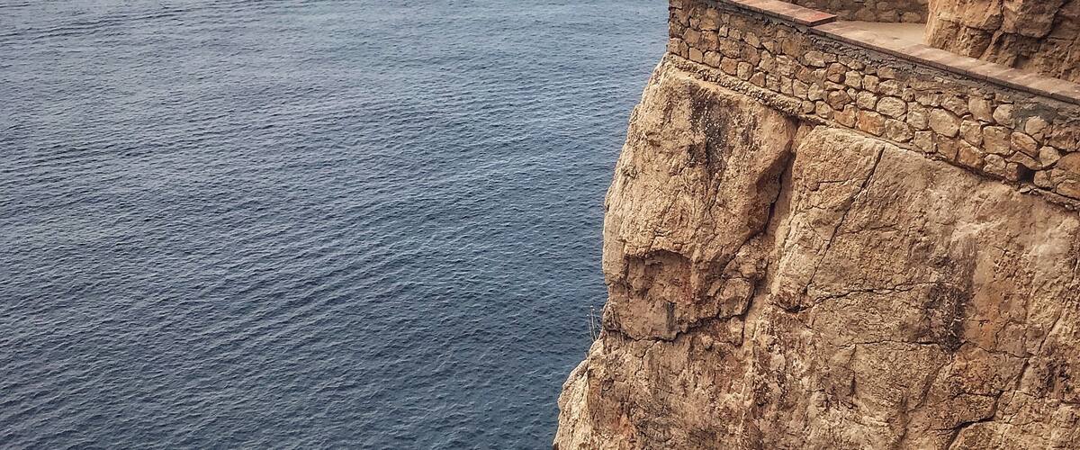 A cliff overlooking the ocean with a stone pathway and two people standing at the edge.
