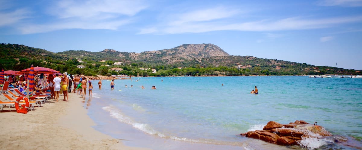 A beach with clear turquoise water, sun loungers, and umbrellas.