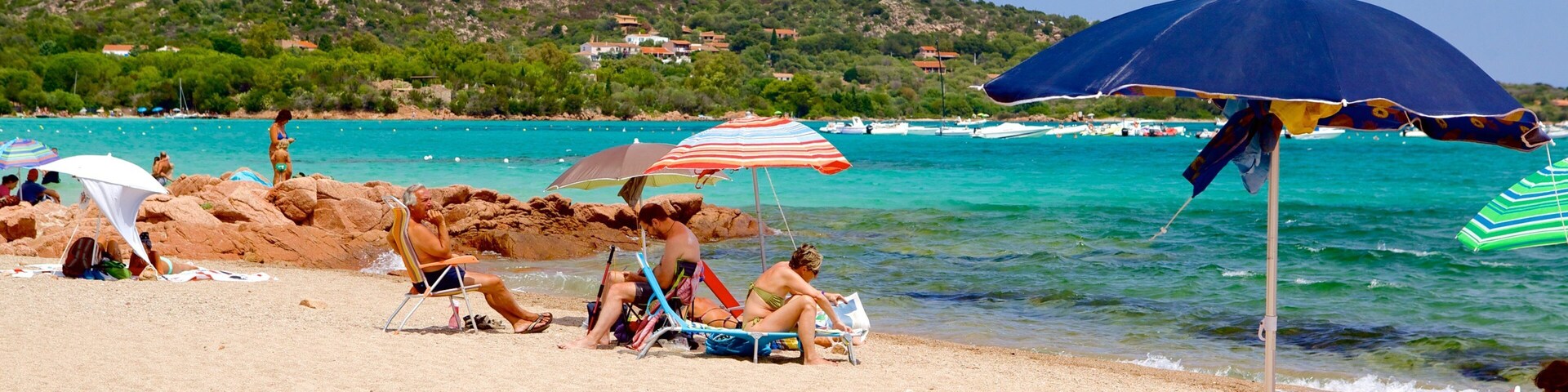 Uma praia com pessoas relaxando sob guarda-sóis, uma montanha ao fundo e água turquesa cristalina.