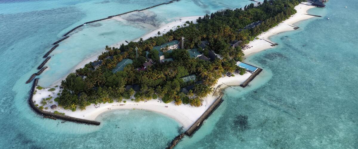An aerial view of a tropical island with a white sandy beach, dense palm trees, and clear turquoise waters.