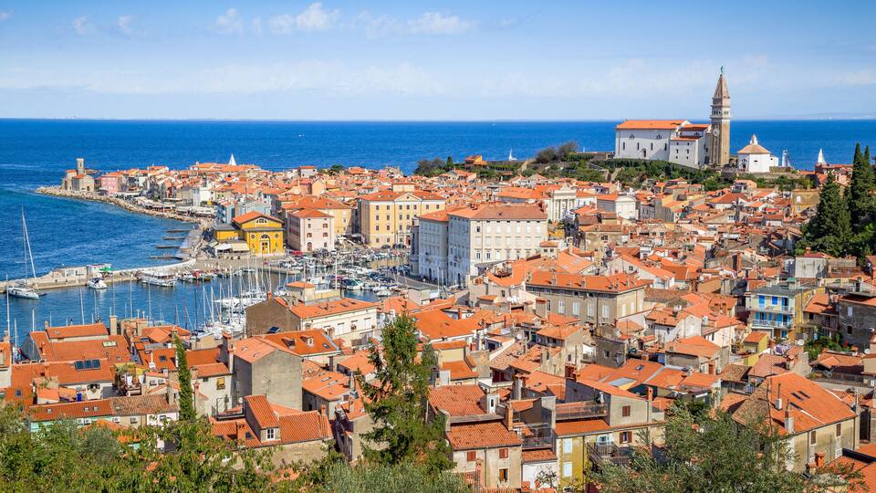 A coastal town with red-roofed buildings, a marina, and a prominent church with a clock tower.