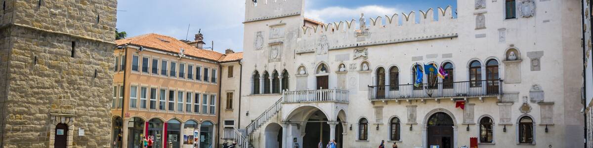 A historic square with a prominent castle-like building featuring arched windows and a balcony.