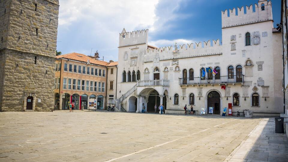 A historic square with a prominent castle-like building featuring arched windows and a balcony.