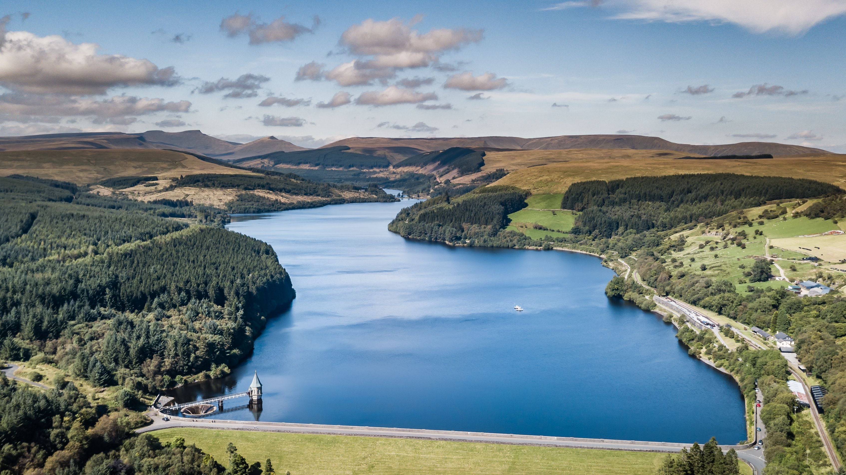A large lake surrounded by hills and forests, with a bridge crossing the water.