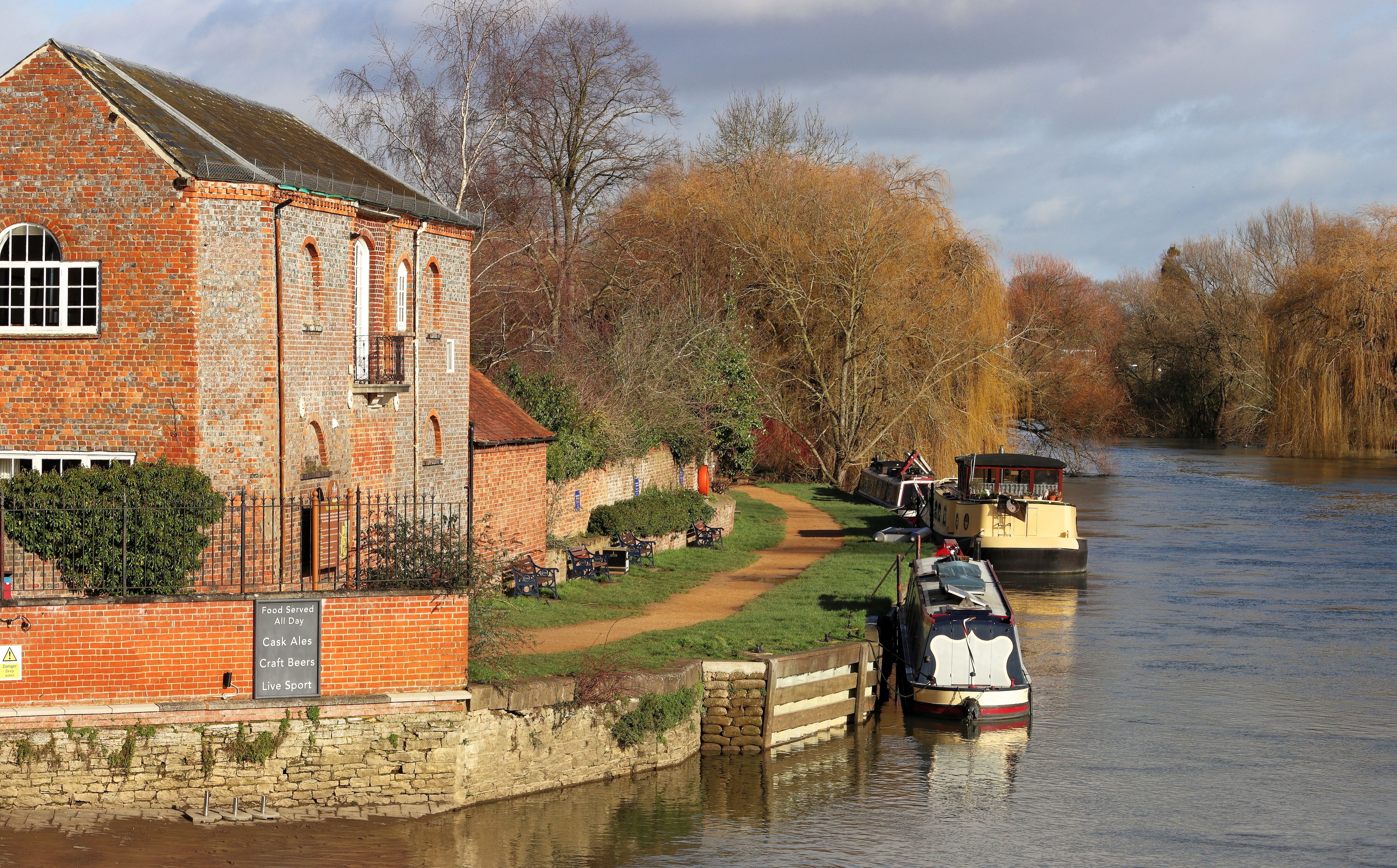 A brick building with a river, boats, and autumn trees.