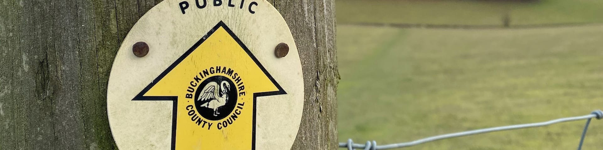 A public footpath sign on a tree with barbed wire.