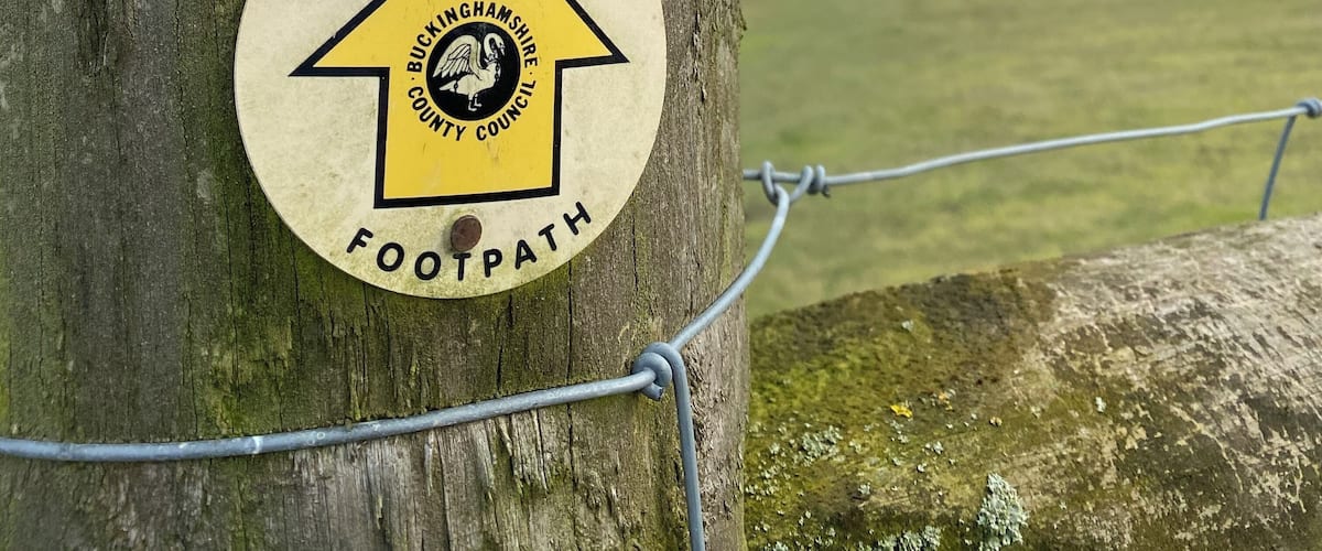 A public footpath sign on a tree with barbed wire.