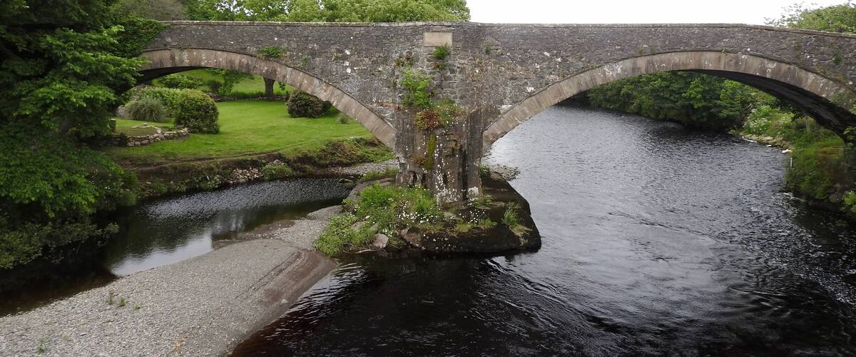 A stone bridge over a river with lush greenery and a well-maintained lawn.