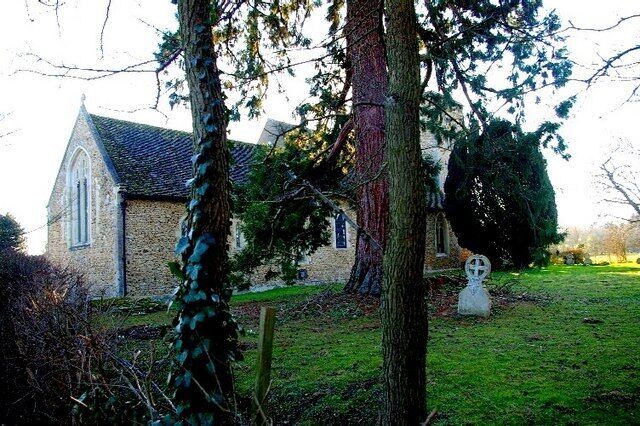A stone church with a steeple, surrounded by trees and a grassy area.