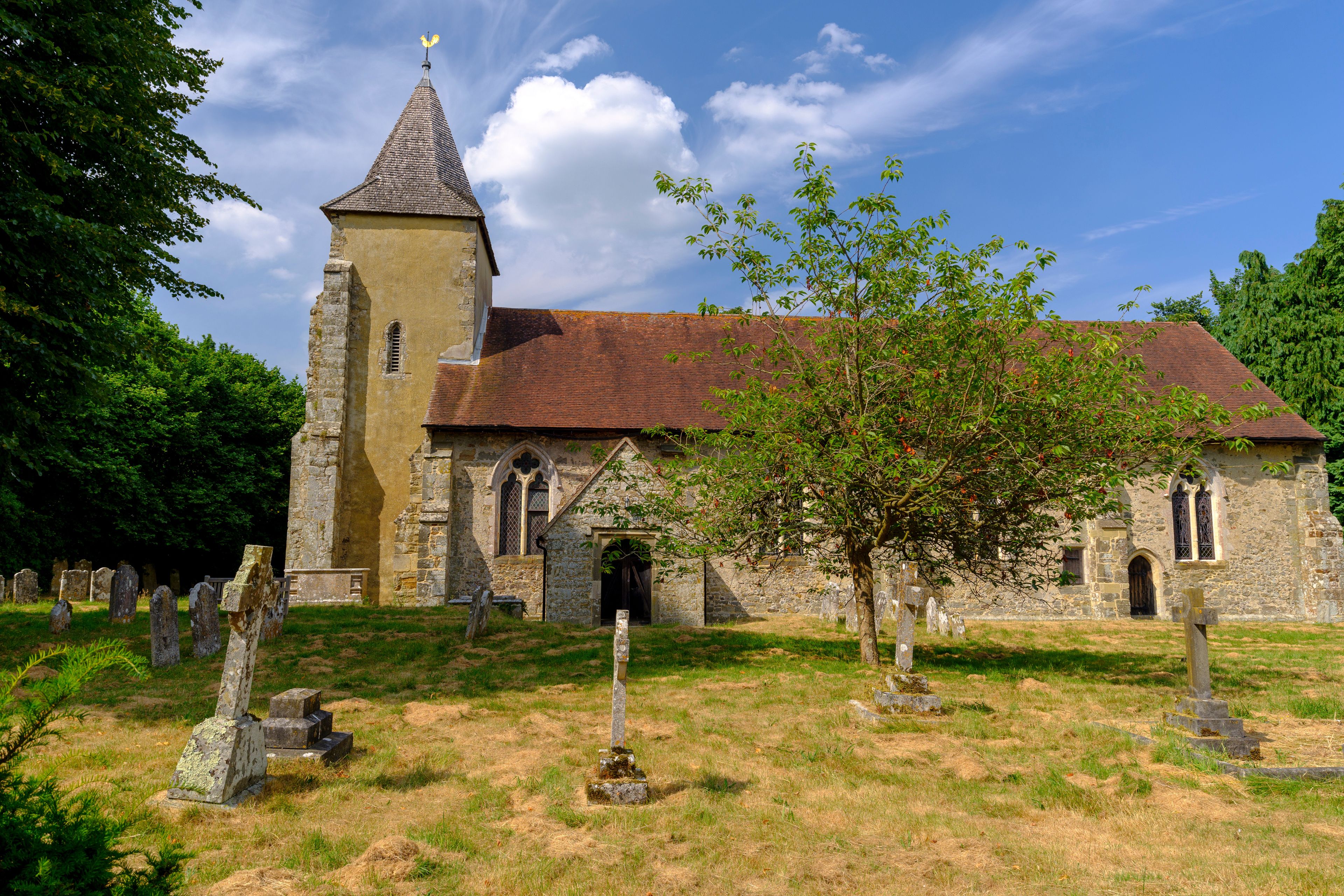 A historic church with a tall tower and a red-tiled roof, surrounded by a cemetery with gravestones.