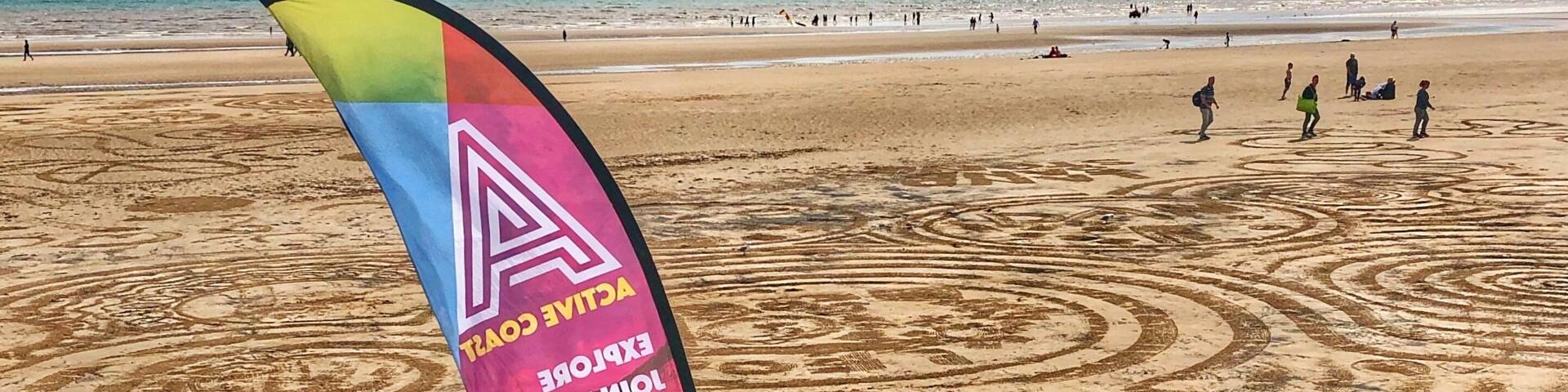 A beach with a colorful flag and circular patterns in the sand.