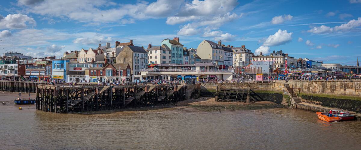 A riverside town with a pier, historic buildings, and a boat on the water.