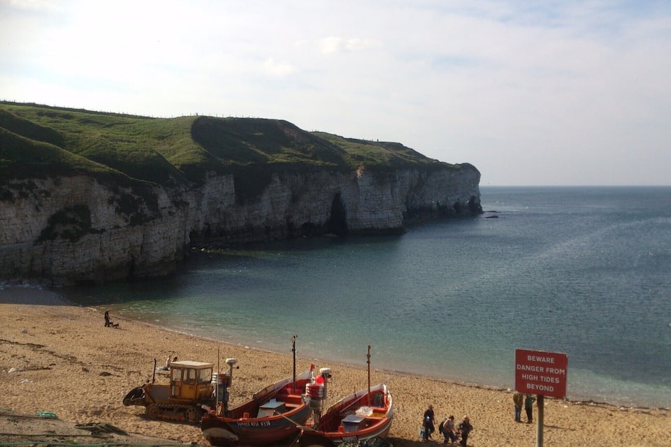 A beach with boats, cliffs, and a warning sign about high tides.