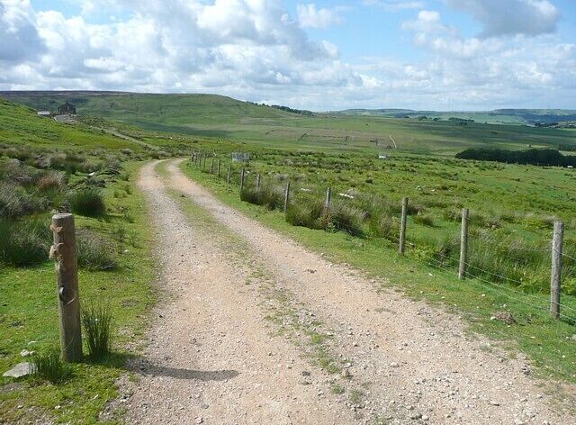 A gravel path in a rural area with green fields and a fence on one side.