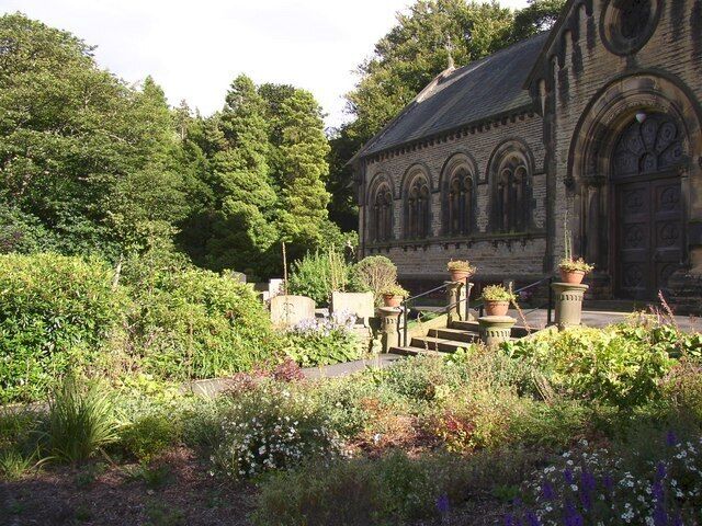A historic building with arched windows and a stone facade, surrounded by a lush garden with various plants and flowers.
