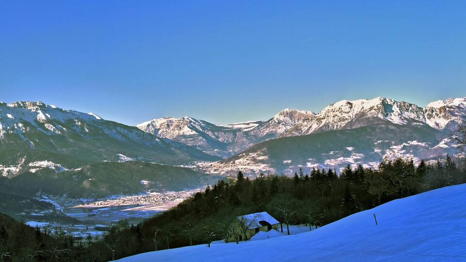 A snow-covered mountain range with a valley and a small cabin.