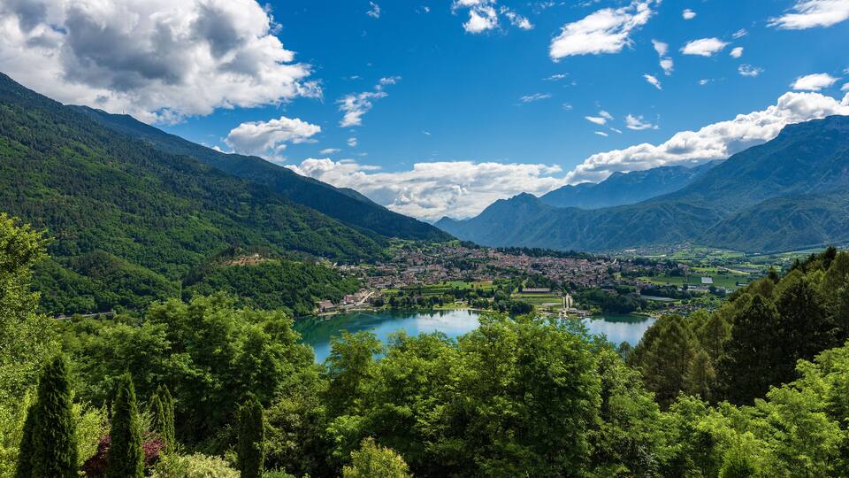 A mountainous landscape with a lake, dense greenery, and a small town in the valley.