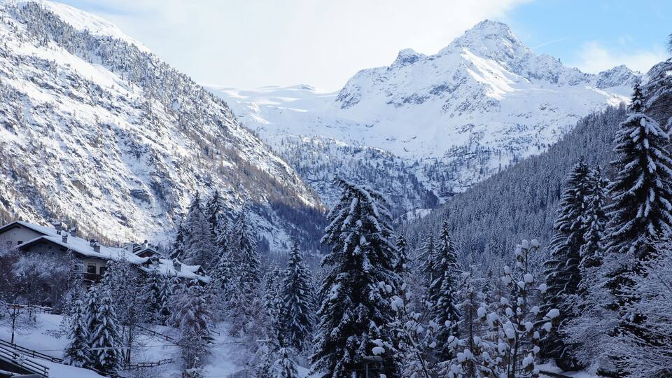 A snow-covered mountain landscape with a cabin and evergreen trees.