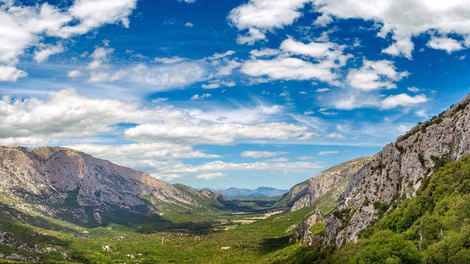 A mountainous landscape with a valley, rocky cliffs, and scattered greenery.