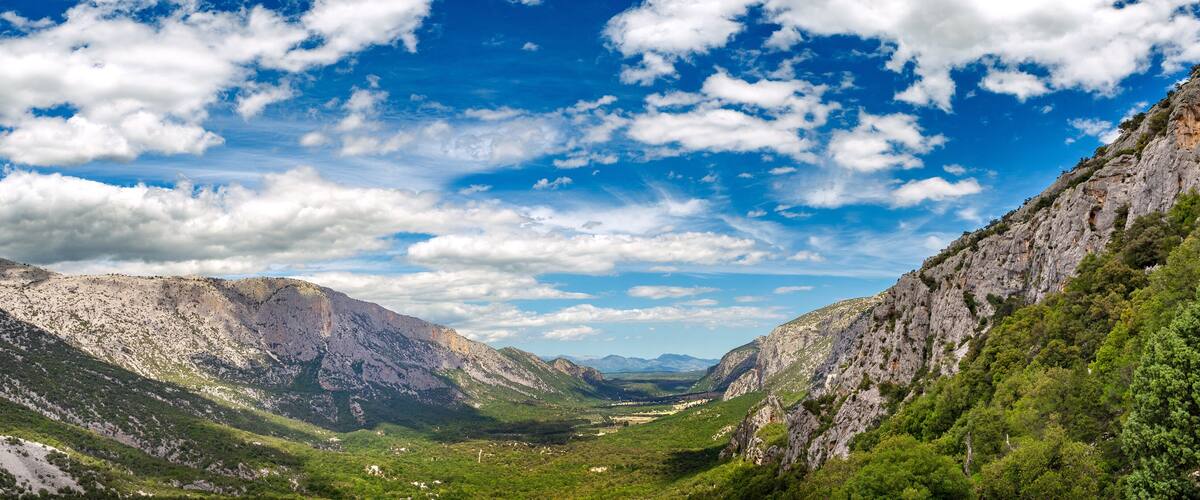A mountainous landscape with a valley, rocky cliffs, and scattered greenery.