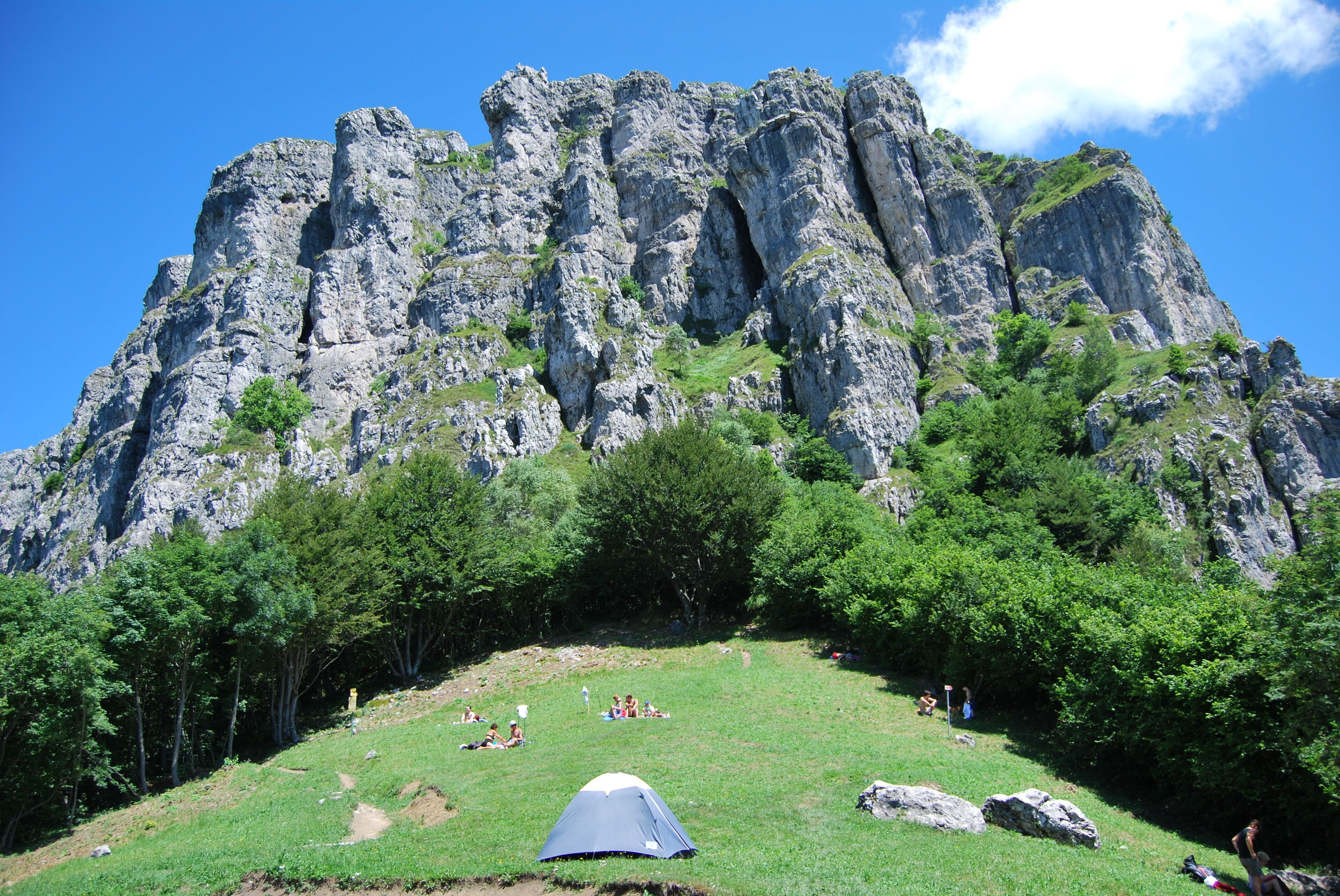 A rocky mountain with a grassy area and a tent.