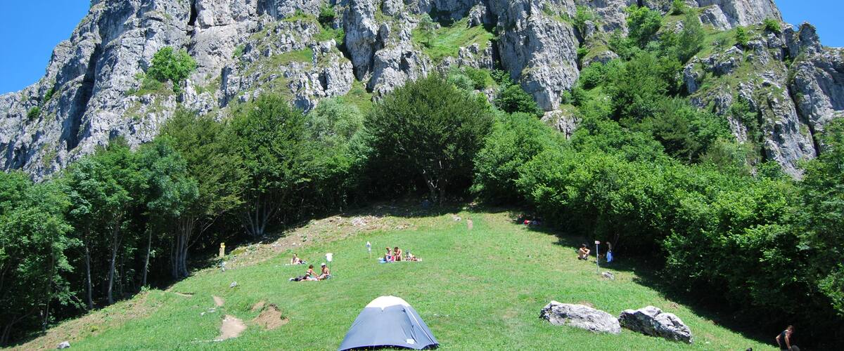 A rocky mountain with a grassy area and a tent.