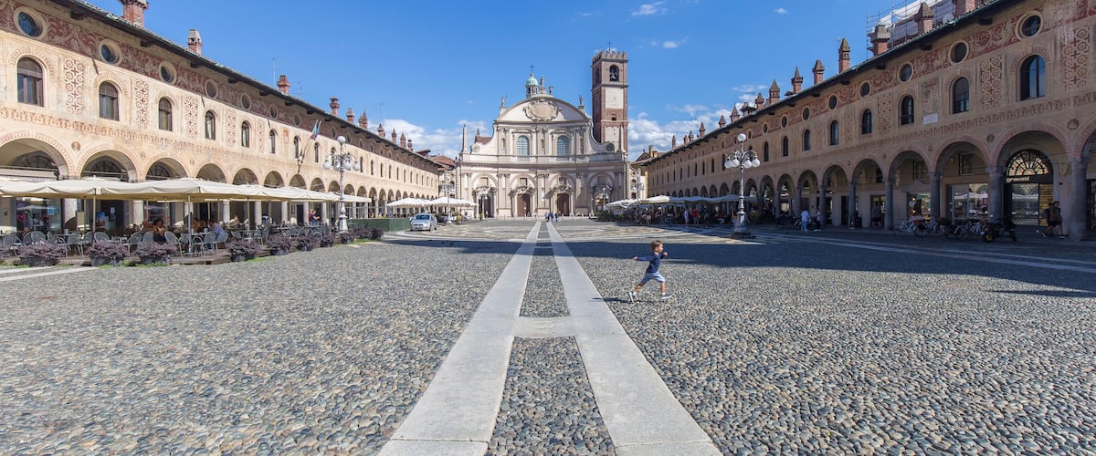 A historic square with a central building featuring a dome and bell tower, flanked by ornate buildings and a cobblestone street.