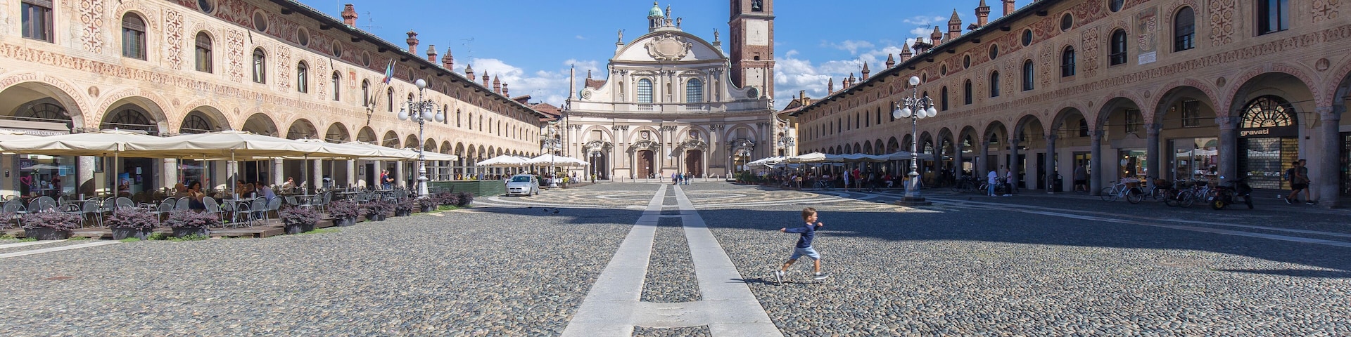 A historic square with a central building featuring a dome and bell tower, flanked by ornate buildings and a cobblestone street.