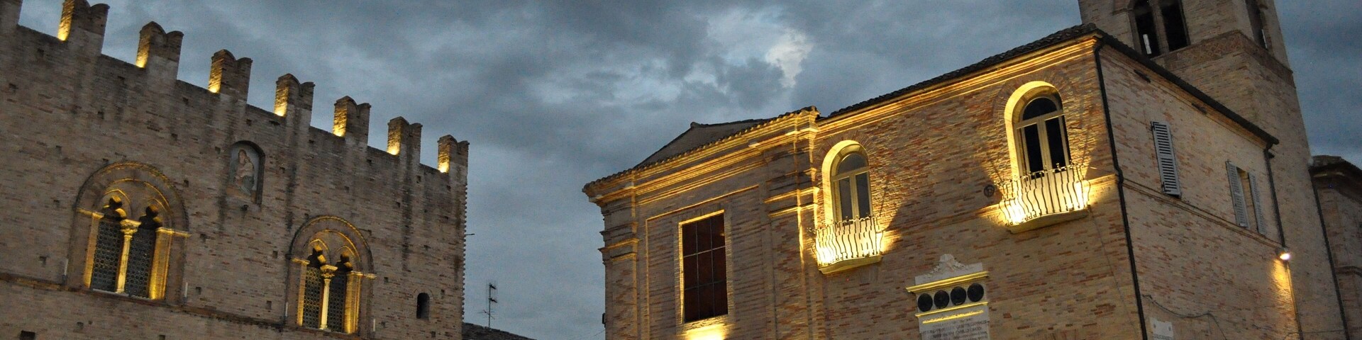A historic building with arched windows and a tower, illuminated by warm lights.
