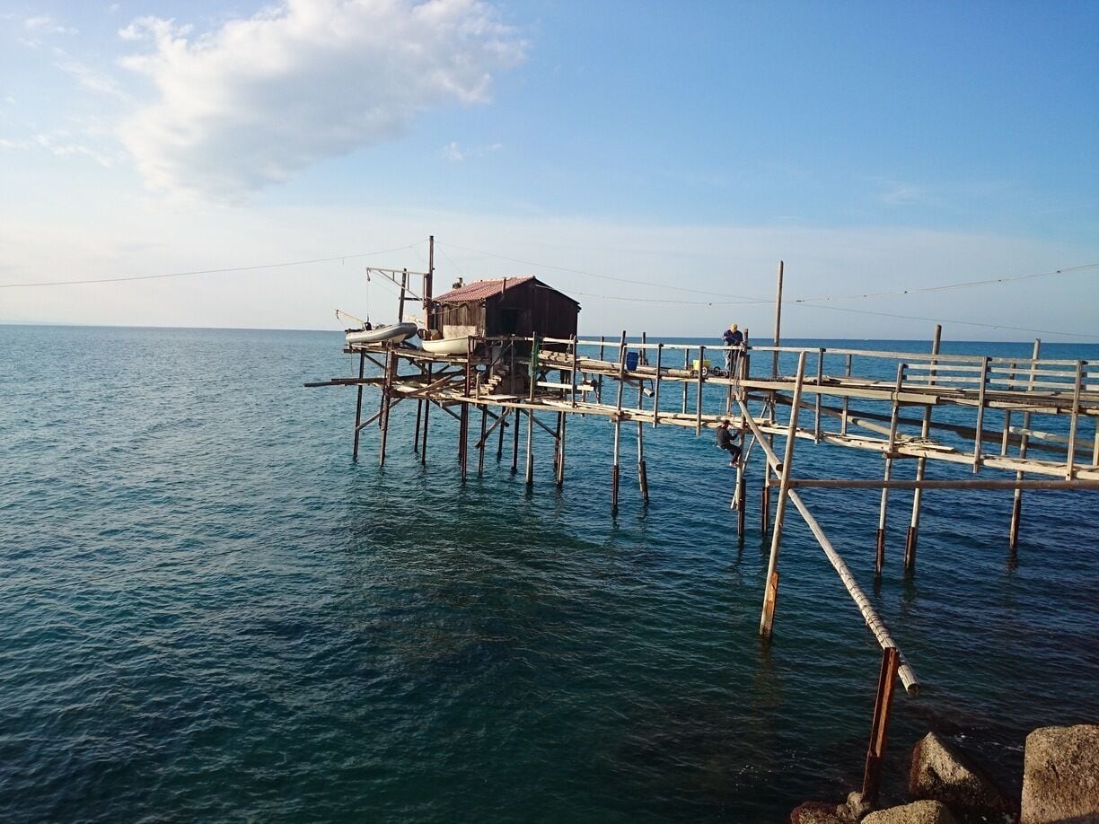 Un muelle de madera que se adentra en un mar tranquilo, con un pequeño edificio al final.
