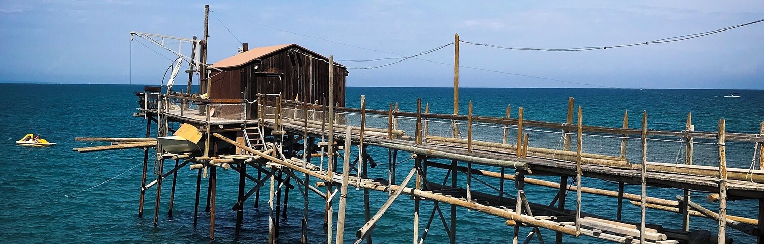 Un muelle de madera que se adentra en el mar, con un pequeño edificio en su extremo.