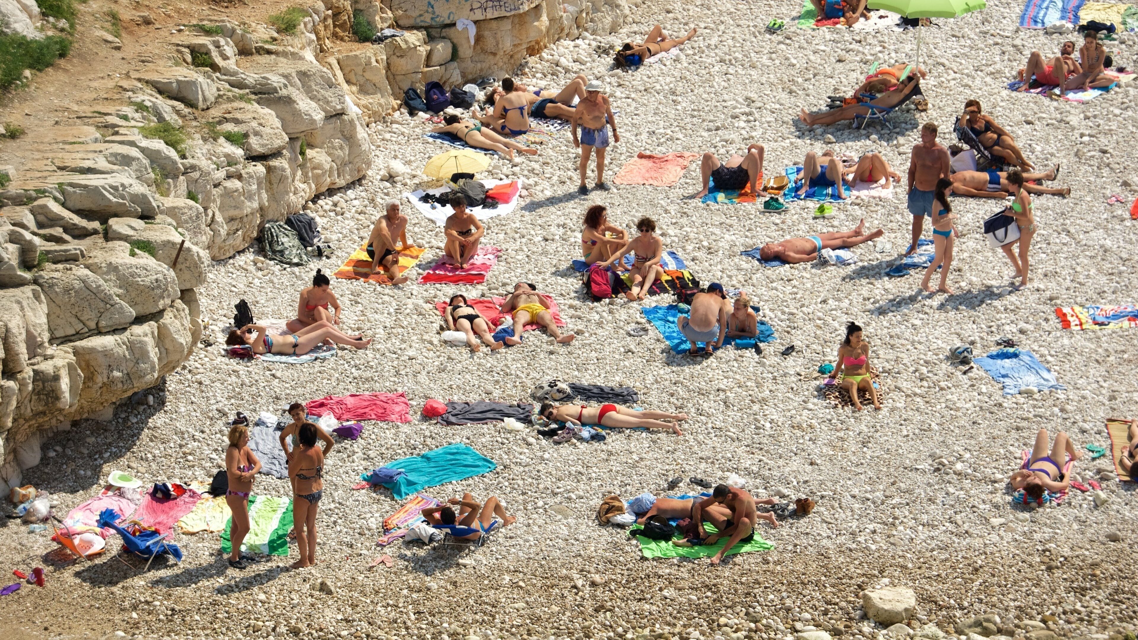 A crowded pebble beach with people sunbathing and relaxing.