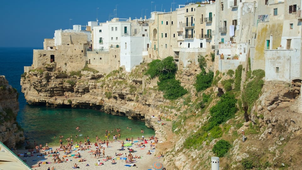 A coastal town with a rocky shoreline, a crowded beach, and white buildings with balconies.