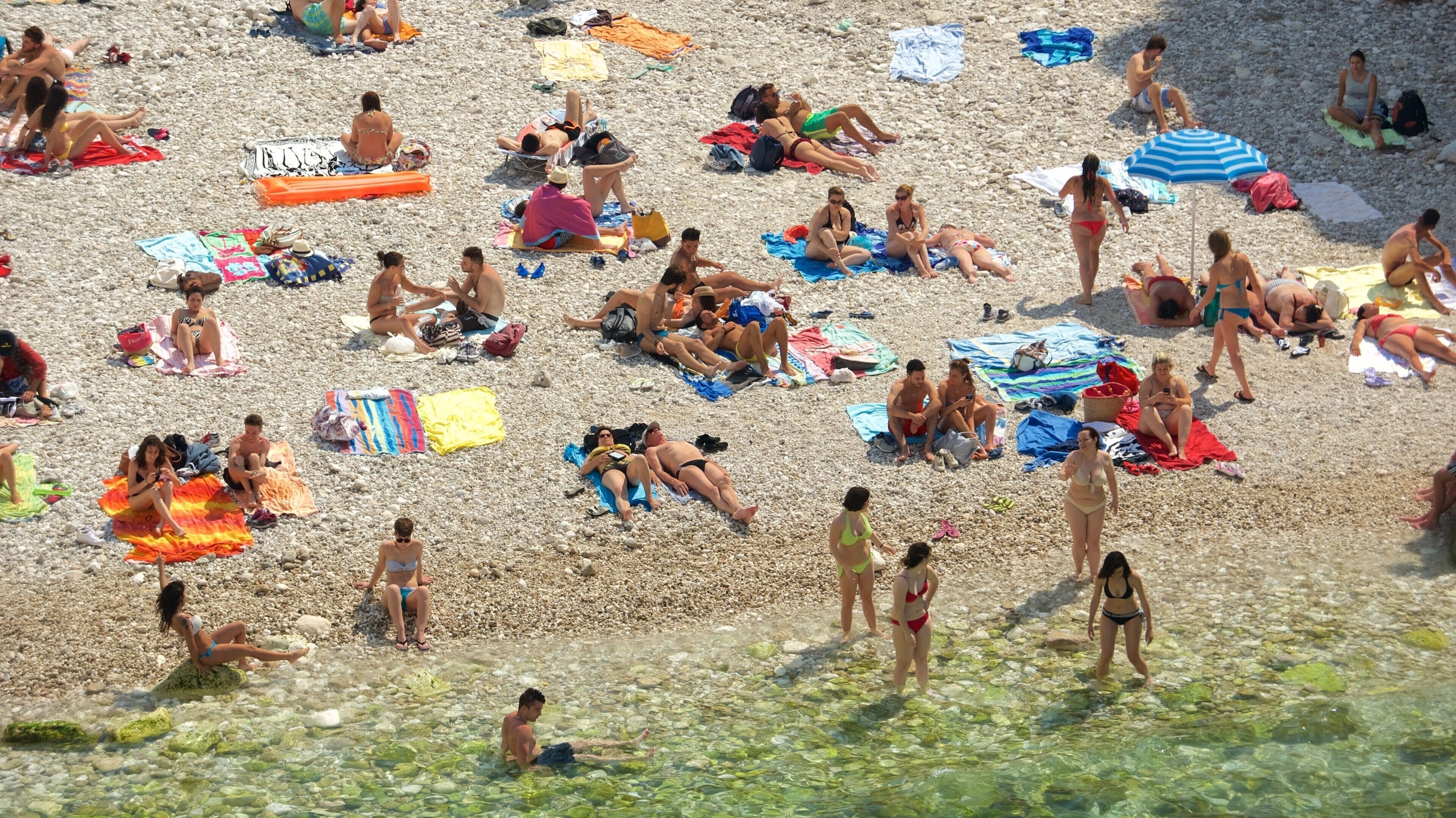 A crowded pebble beach with people sunbathing and swimming.