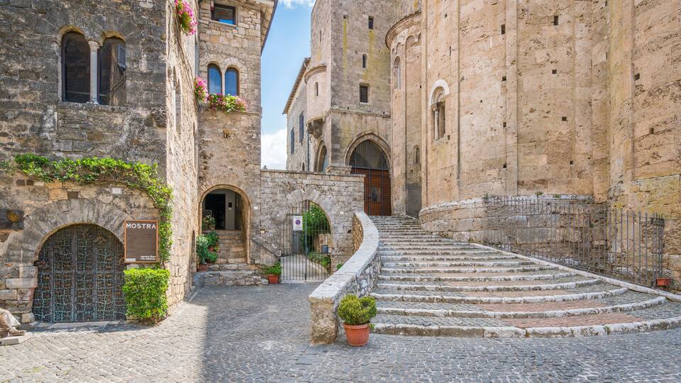 A cobblestone street leading to a historic building with a sign reading "MOSTRA."