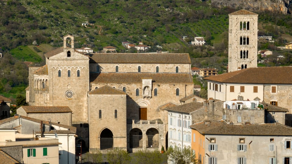 A historic church with a bell tower and a clock, surrounded by traditional buildings and a hilly landscape.