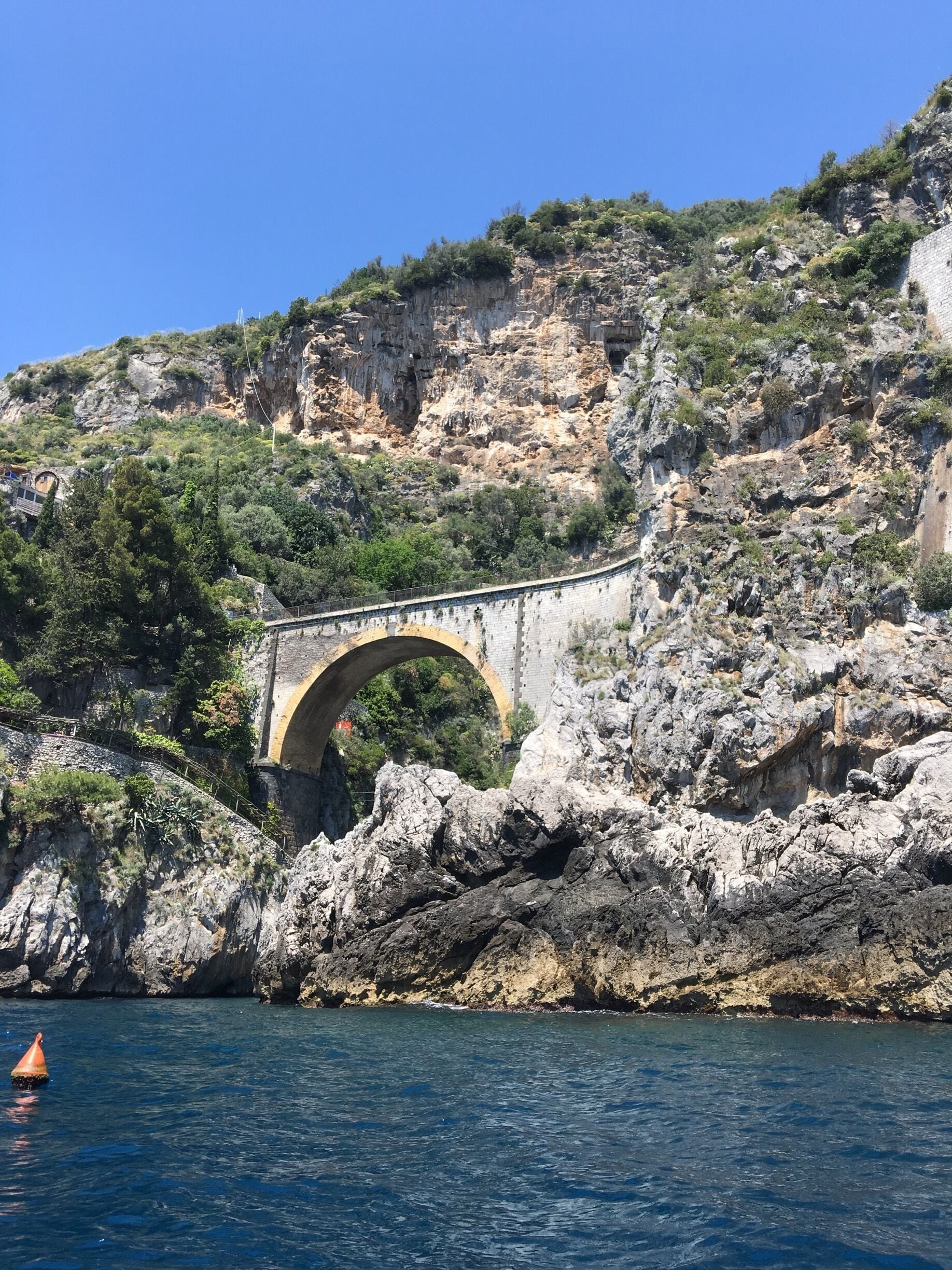 A stone bridge over a rocky coastline with a clear blue sky.