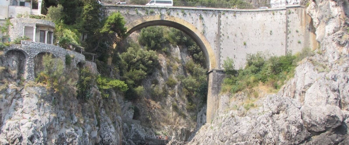 A stone bridge over a river, surrounded by rocky cliffs and greenery.