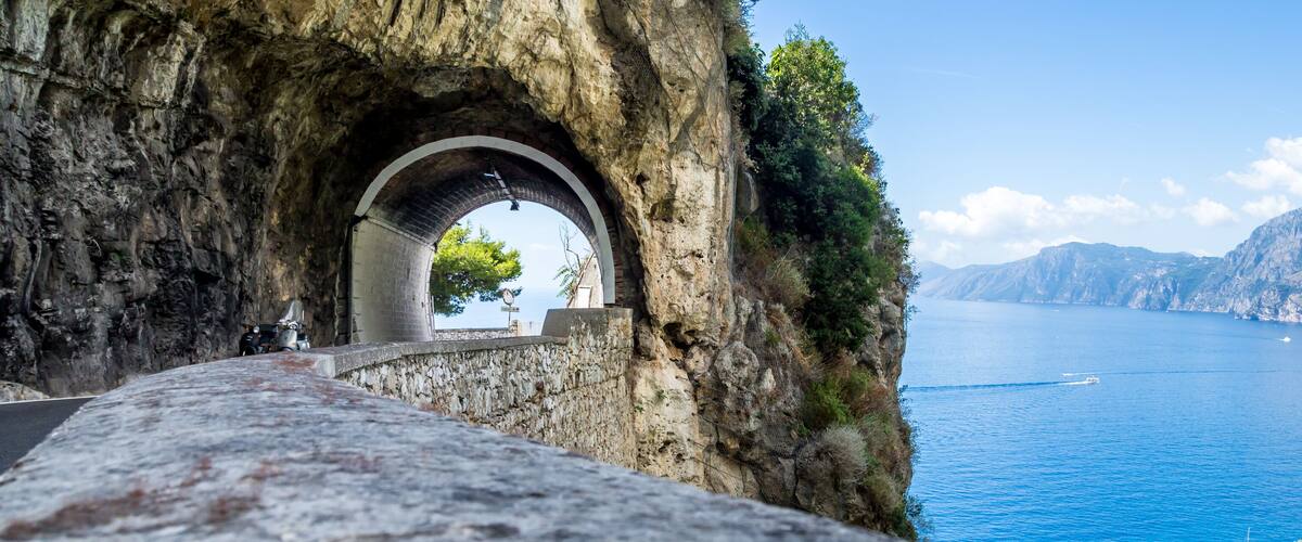 A stone bridge with an archway leading to a coastal view.