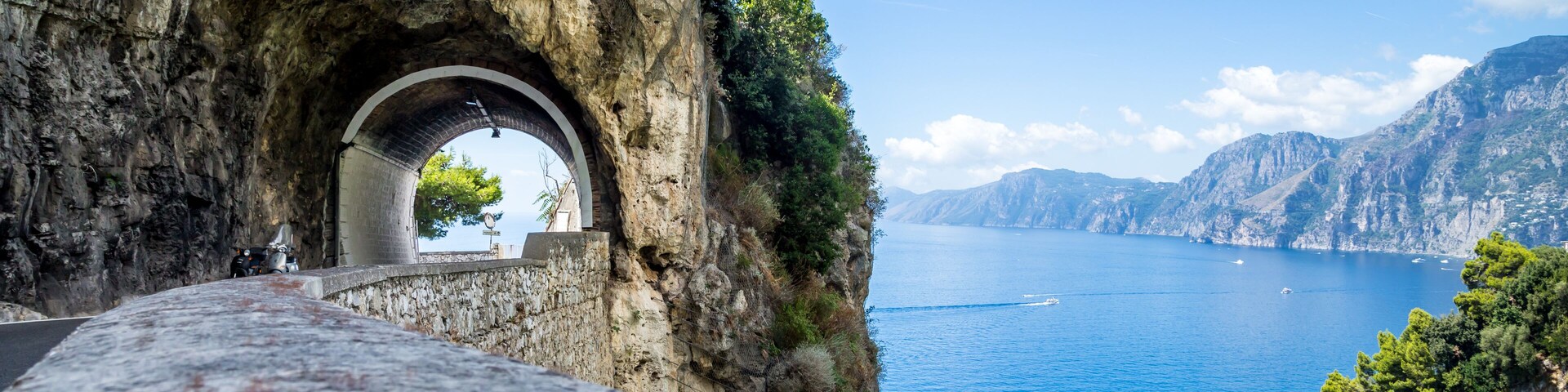 A stone bridge with an archway leading to a coastal view.