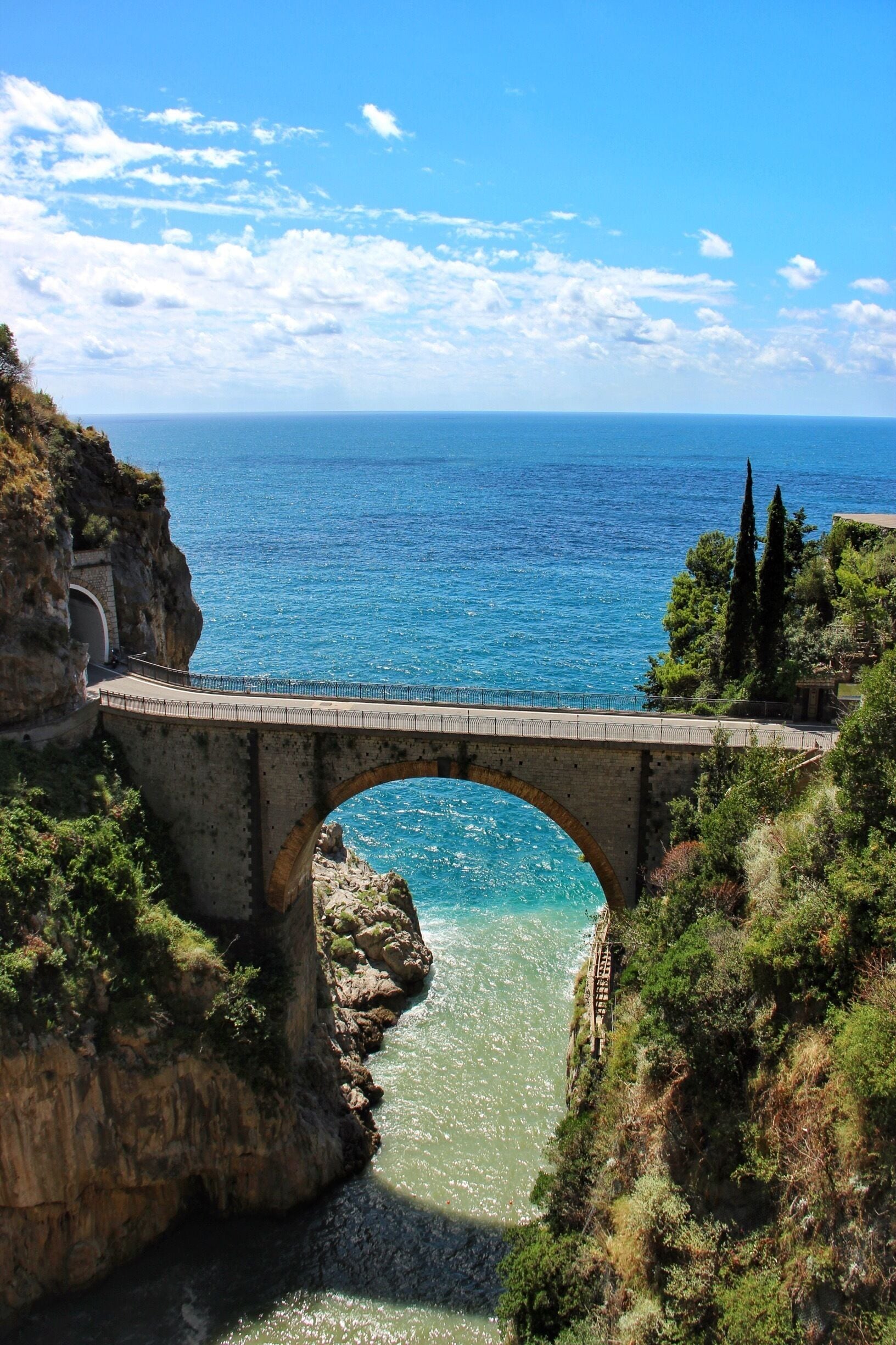 A stone bridge over a narrow water passage with cliffs on either side and a clear blue sky.