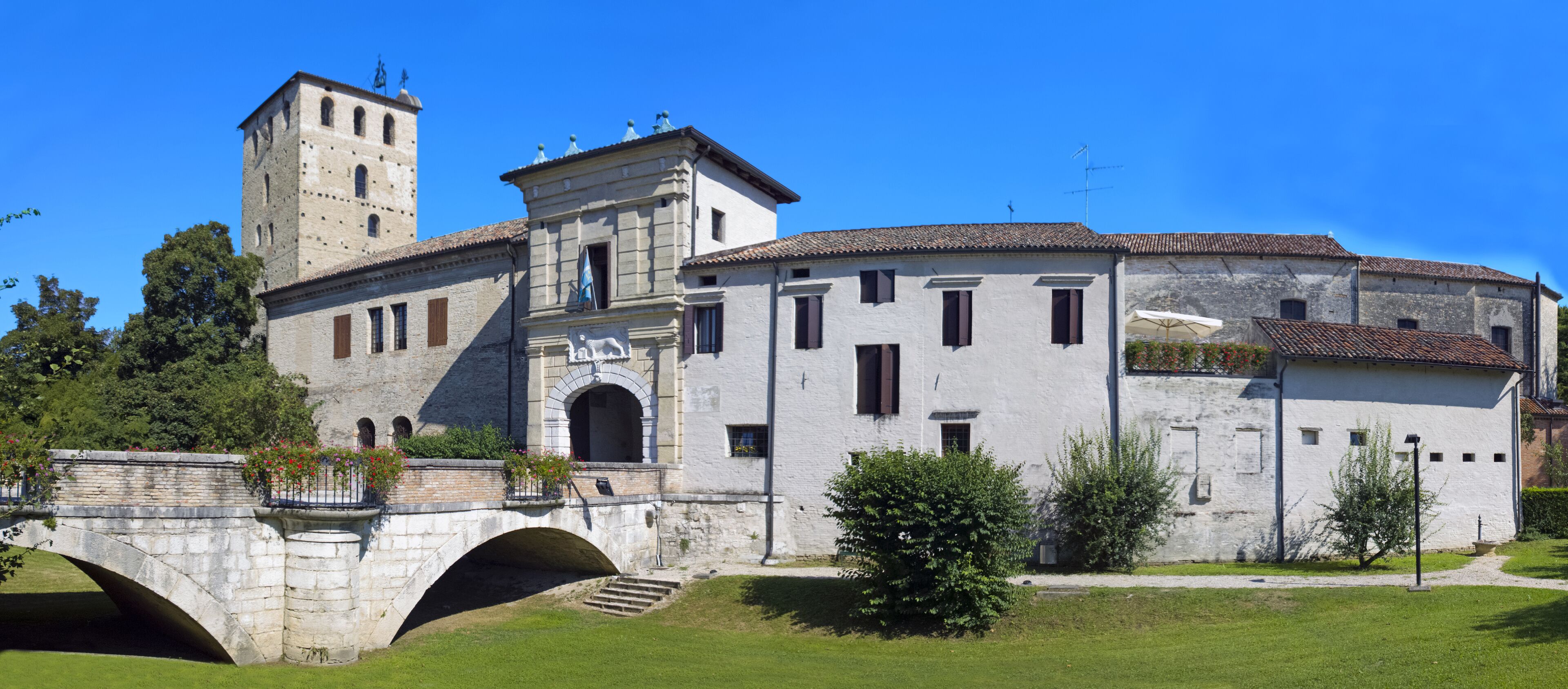 A historic building with a tower, a bridge, and a well-maintained garden.