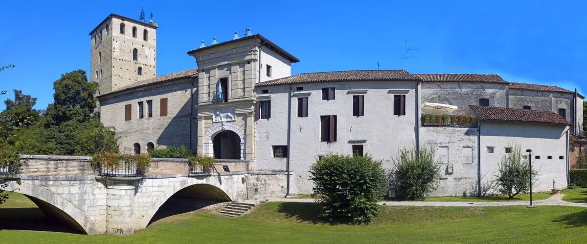 A historic building with a tower, a bridge, and a well-maintained garden.